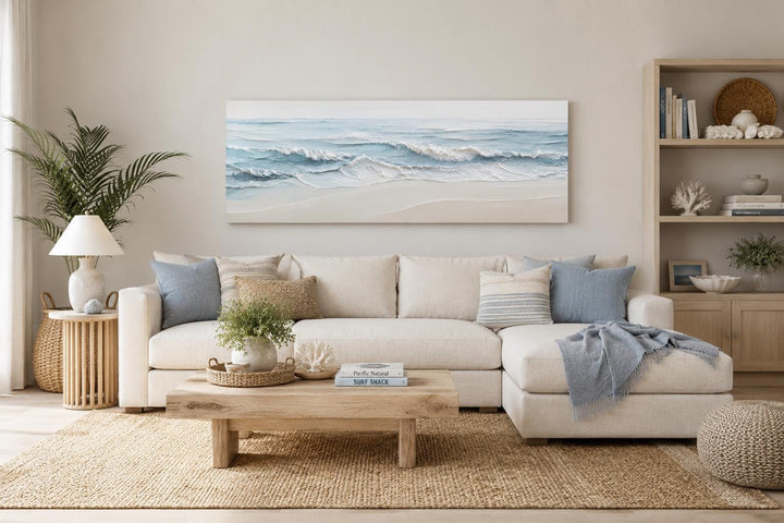 Calm ocean waves canvas print in soft blue and cream tones above a neutral sofa in a coastal room.