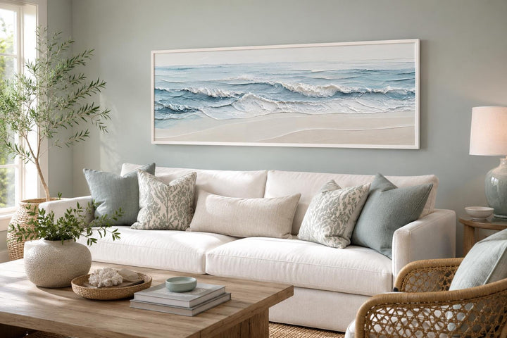 Calm ocean waves canvas wall art in soft blue and cream tones above a white sofa.