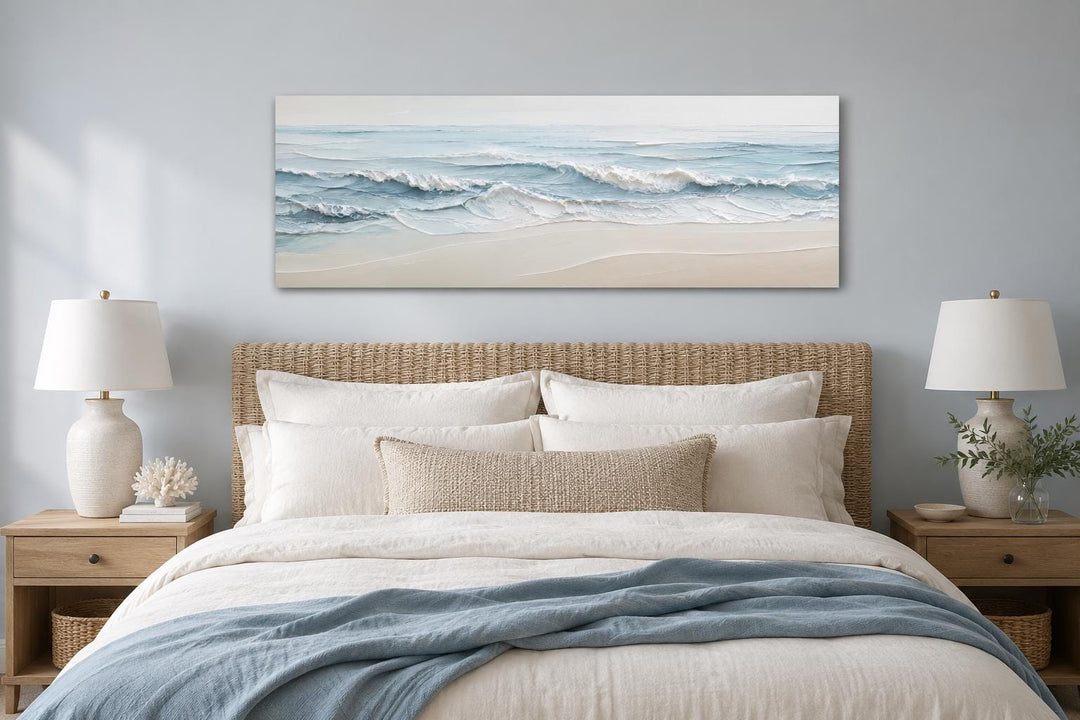 Calm ocean waves canvas wall art in soft blue and cream tones hanging above a coastal style bed.