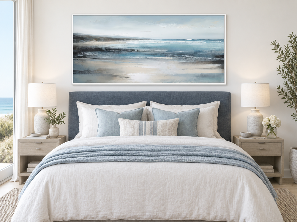 Minimalist blue and gray ocean framed canvas wall art hanging above a bed in a coastal bedroom.