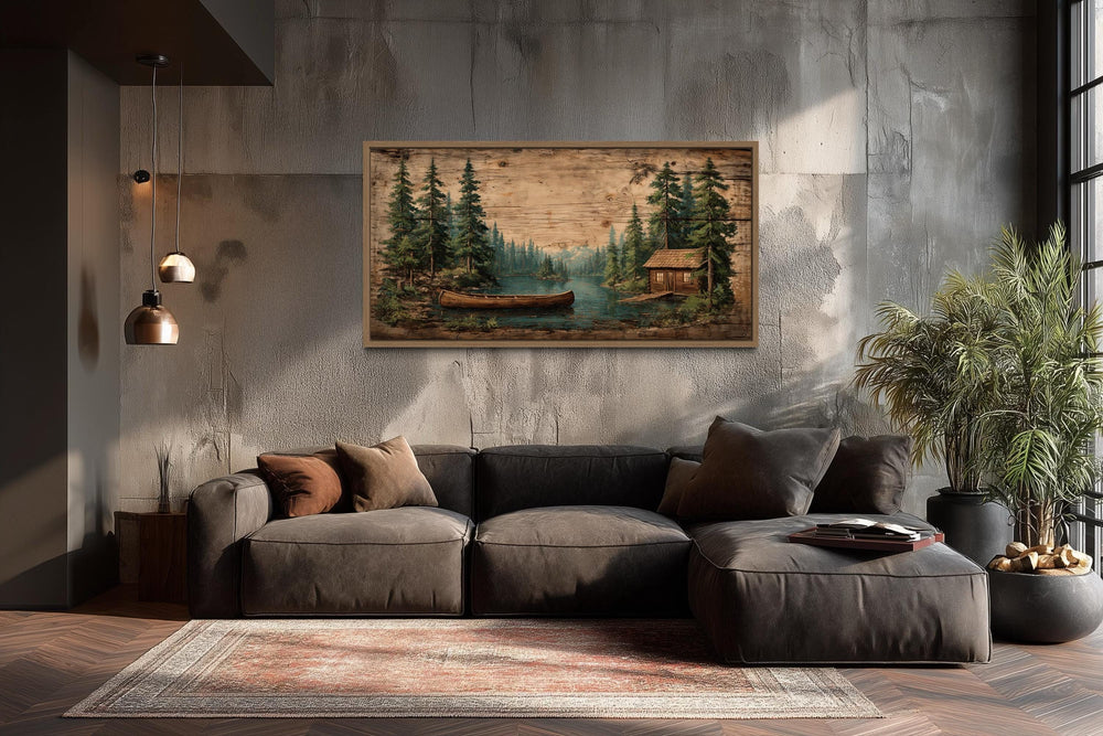 Canoe in the lake and pine forest scene canvas wall art hanging above a dark sofa in a rustic room.