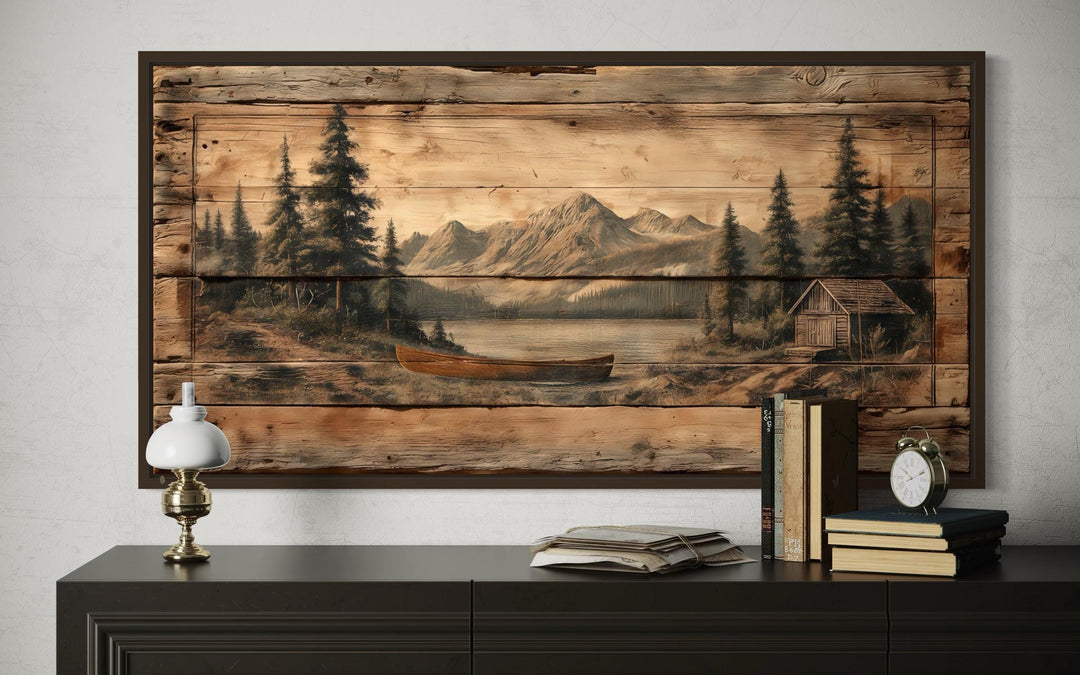 Canoe on mountain lake canvas wall art with a rustic wood-plank style print above a dark sideboard.