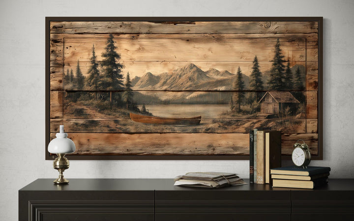 Canoe on mountain lake canvas wall art with a rustic wood-plank style print above a dark sideboard.