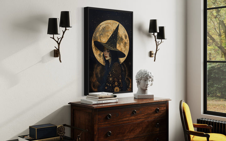Framed wall art of a celestial witch in a starry hat against a large full moon above a dresser.