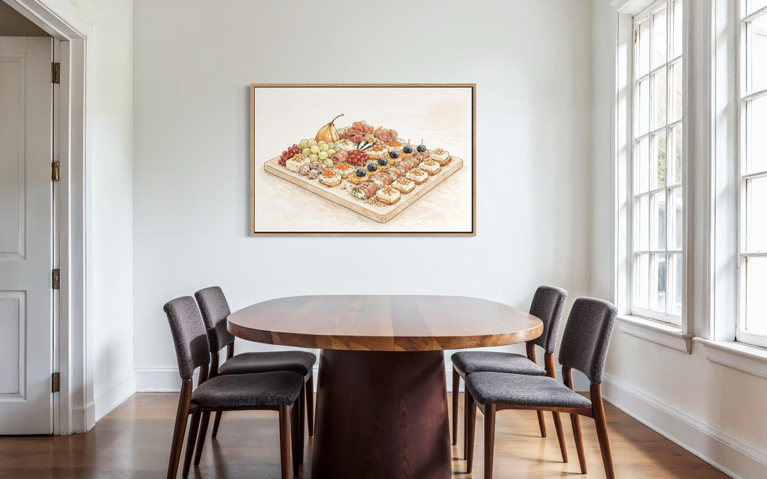 A framed canvas print of a charcuterie board hangs in a modern dining room with a round wood table.
