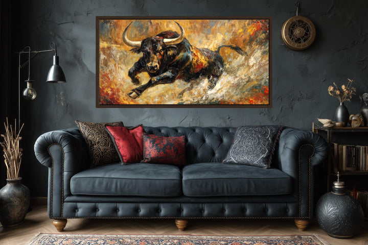Charging bull canvas print in a bold abstract style with gold and red tones over a dark sofa.