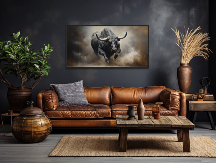 Framed charging bull canvas print hanging above a brown leather sofa in a rustic living room.