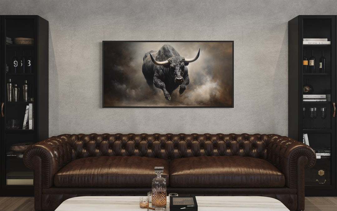 Charging bull framed canvas print centered above a brown leather sofa in a rustic man cave.