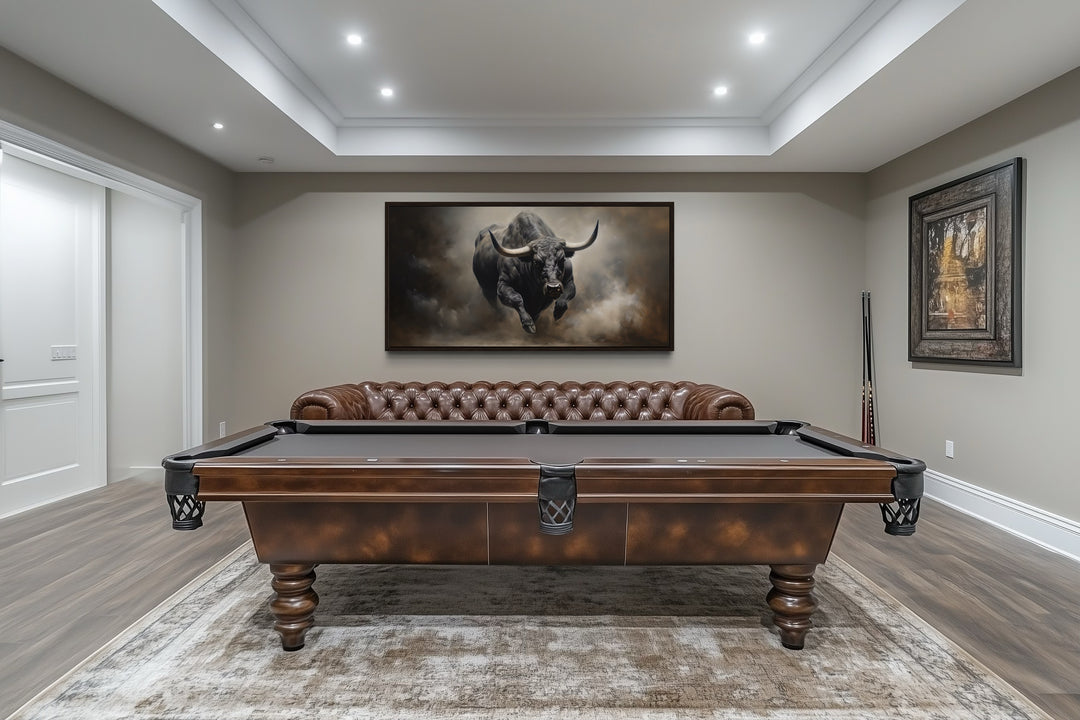 Framed canvas print of a charging bull hanging in a rustic man cave above a brown leather sofa.