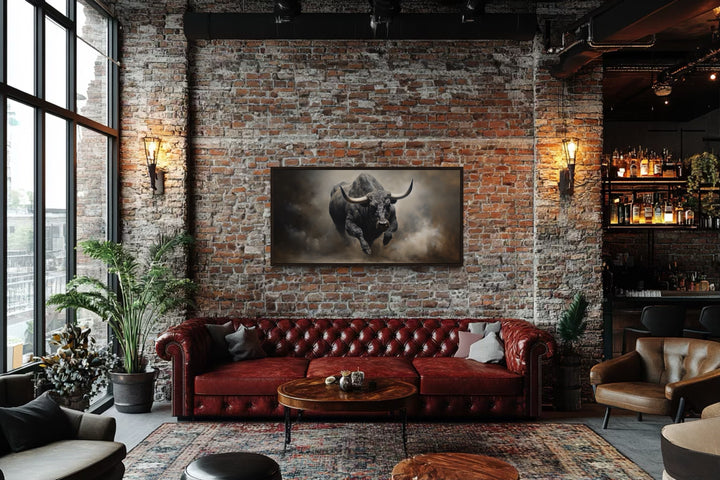 Charging bull framed canvas print on a brick wall above a red leather sofa in a rustic room.