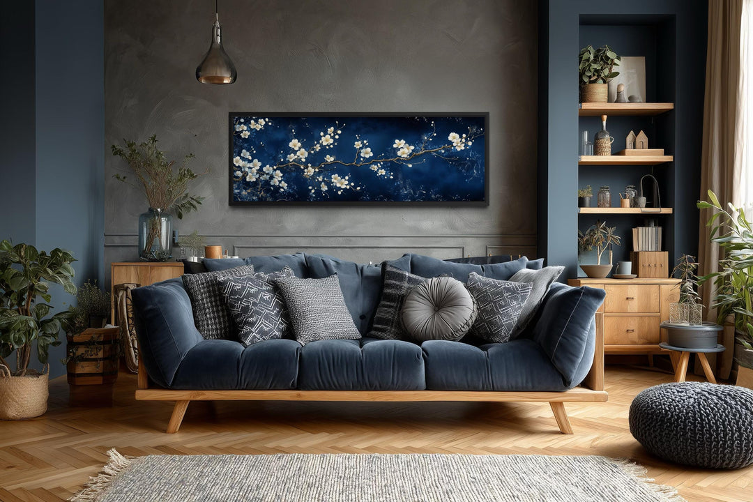 Panoramic cherry blossom wall art with white flowers on a navy blue background above a blue sofa.