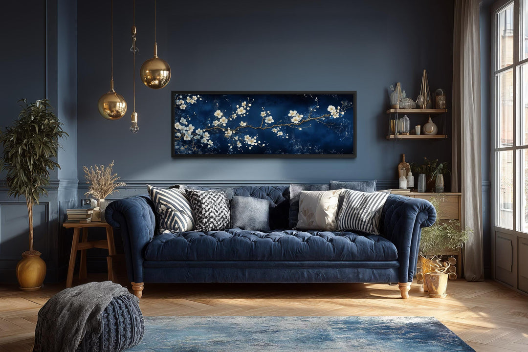 Panoramic cherry blossom canvas print with white flowers on a navy blue background above a sofa.