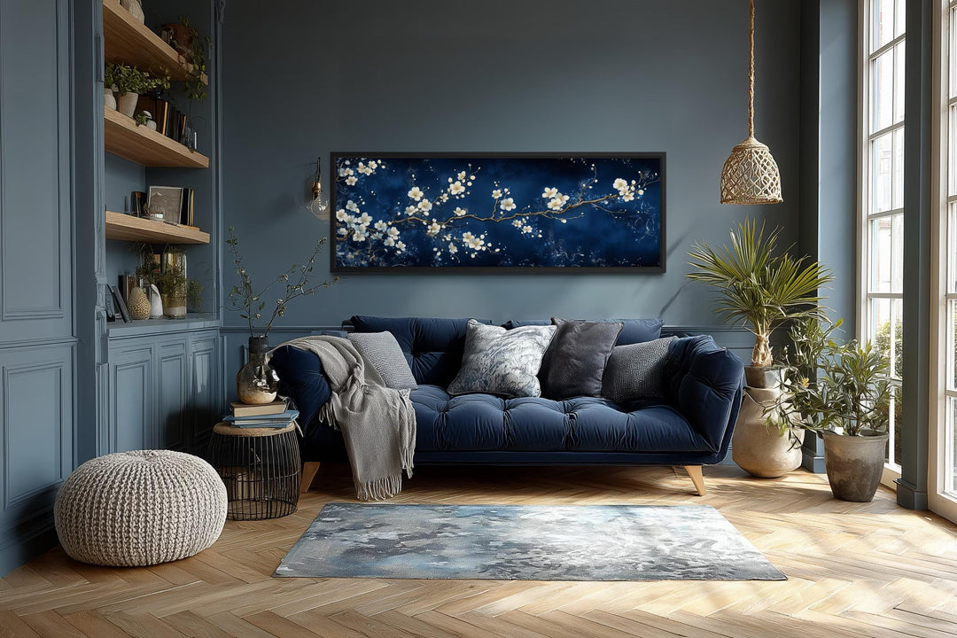 Panoramic cherry blossom wall art with white flowers on a navy blue background in a modern room.