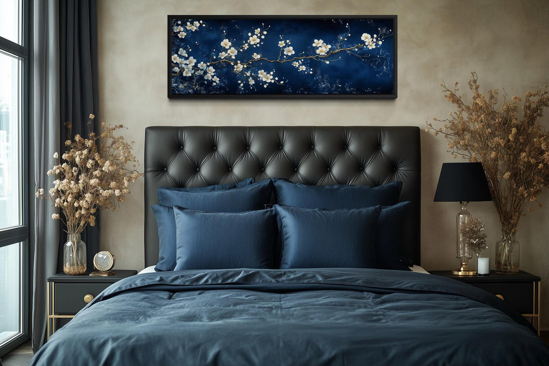 Panoramic cherry blossom canvas print with white flowers on a navy blue background above a bed.