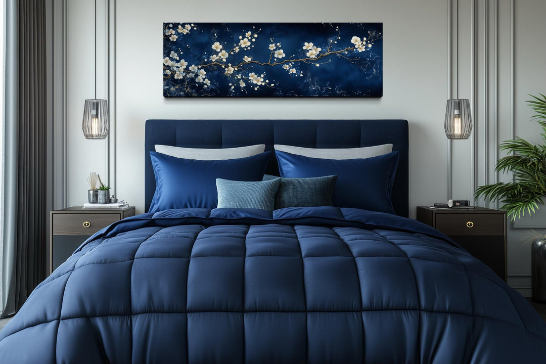Panoramic cherry blossom canvas print with white flowers on a navy blue background above a bed.