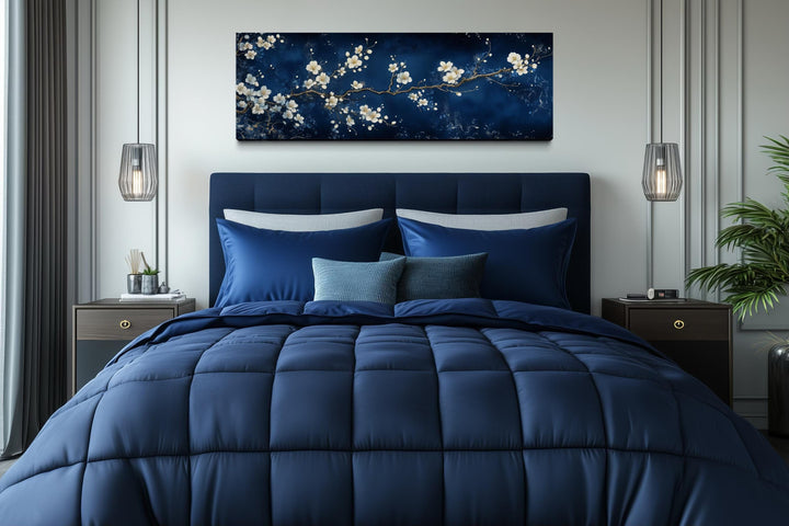 Panoramic cherry blossom canvas print with white flowers on a navy blue background above a bed.