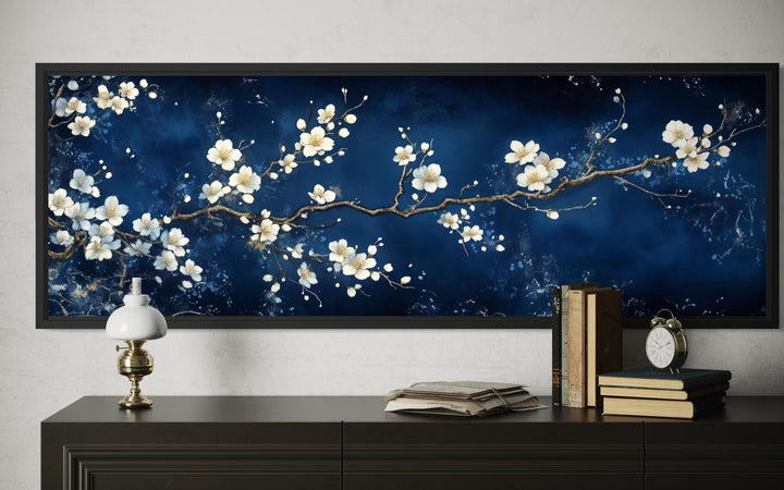 Panoramic cherry blossom wall art with white flowers on a navy blue background above a dark dresser.