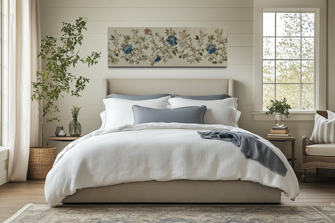 Long horizontal Chinoiserie floral botanical canvas art in blue and beige above a neutral bed.