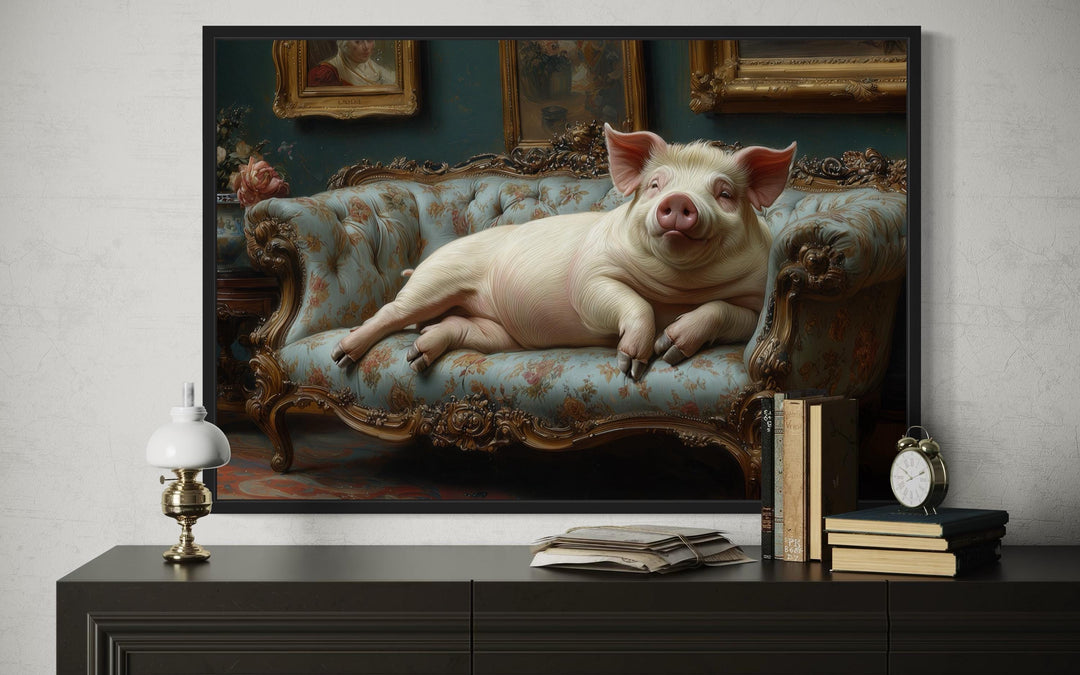 Framed Victorian-style canvas art of a large pig lounging on a blue tufted couch above a sideboard.