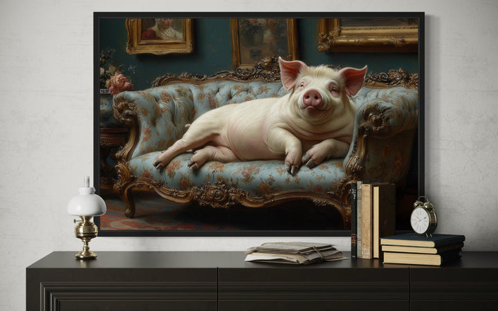 Framed Victorian-style canvas art of a large pig lounging on a blue tufted couch above a sideboard.