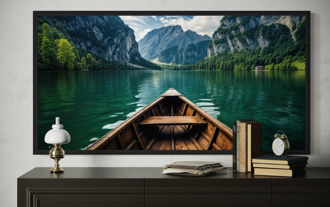 Framed canvas art of a wooden canoe on an emerald green lake with mountains and lush trees.