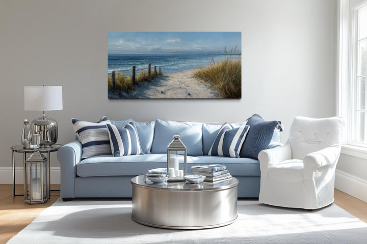 Horizontal canvas print of a coastal beach path with dunes and ocean waves above a blue sofa.