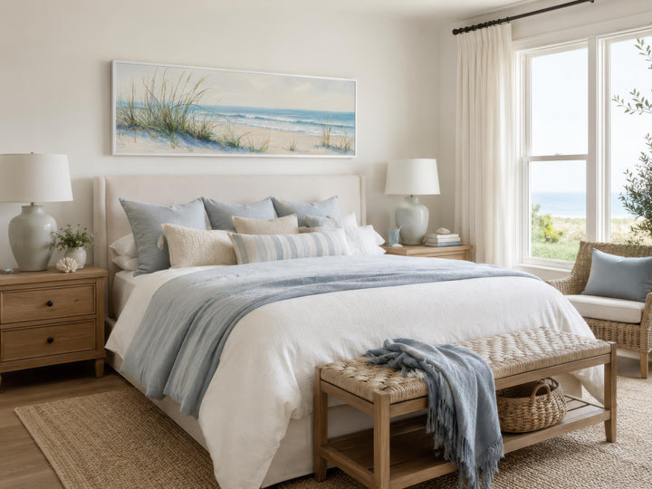 Wide horizontal canvas print of sandy beach dunes and ocean above a bed in a coastal bedroom.