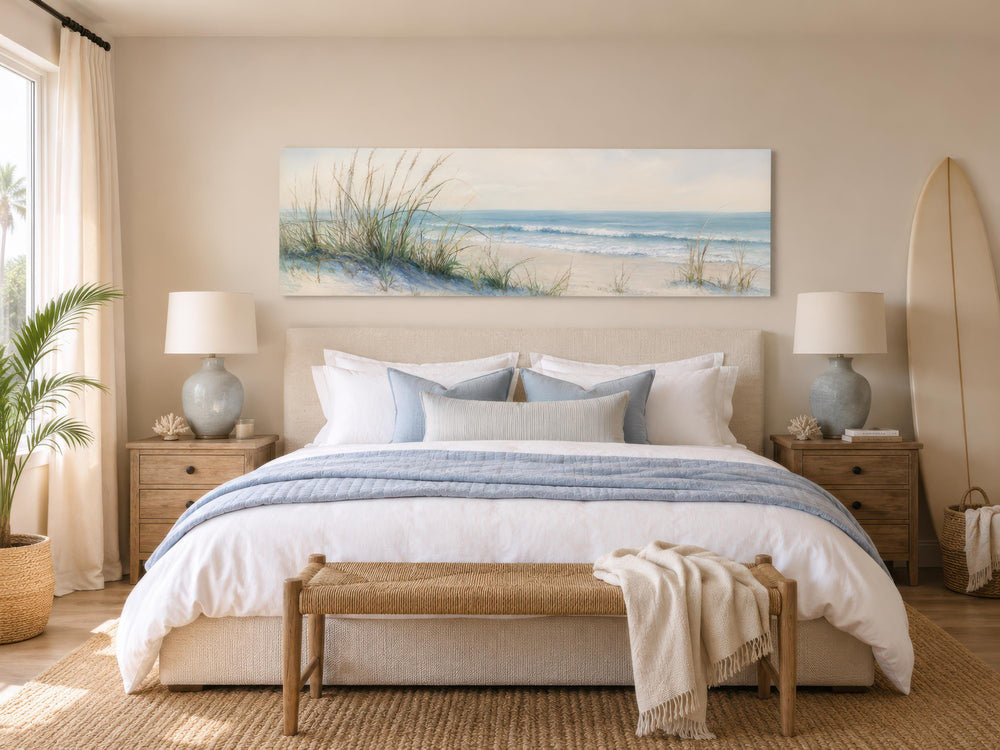 Wide horizontal canvas print of sandy beach dunes and ocean above a bed in a coastal bedroom.