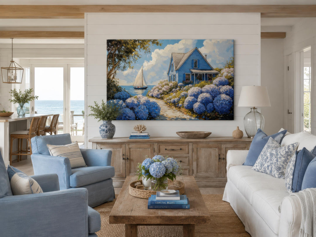 Large coastal canvas print of a blue cottage and sailboat scene above a wooden sideboard.