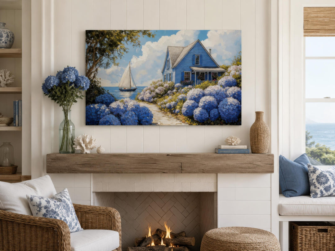 Coastal canvas print of a blue cottage and hydrangeas above a fireplace in a bright living room.