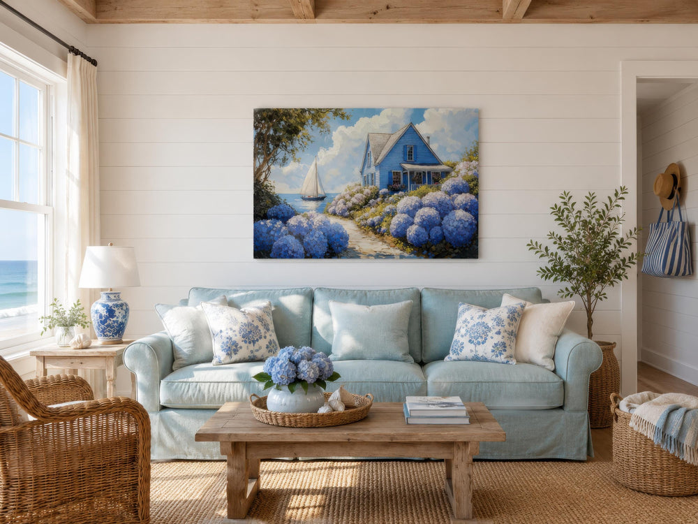 Coastal canvas print featuring a blue cottage, hydrangeas, and a sailboat above a light blue sofa.