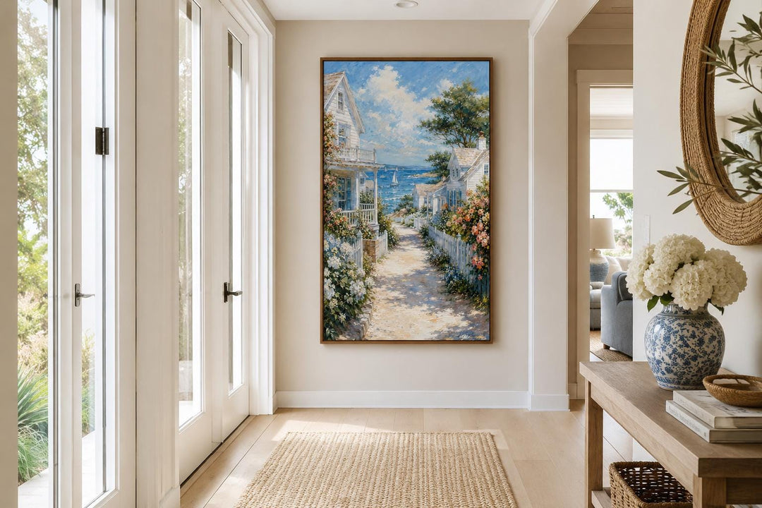 Vertical canvas print of a coastal cottage path leading to the sea, framed in a neutral hallway.