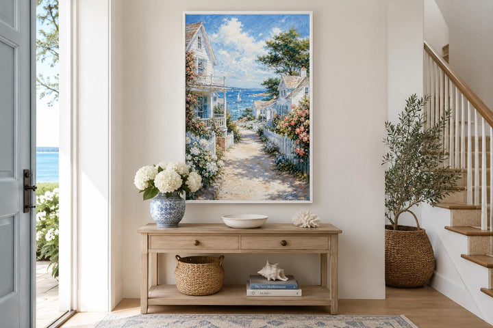 Vertical canvas print of a coastal cottage path leading to the sea, framed above a console table.
