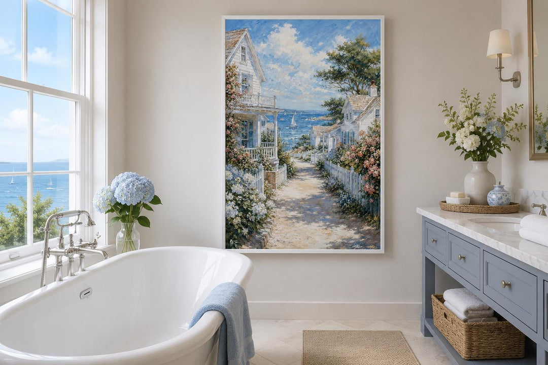 Vertical canvas print of a coastal cottage path leading to the sea, hung in a bright bathroom.
