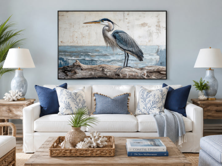 Coastal Heron on Driftwood canvas print above a white sofa with blue and white patterned pillows.