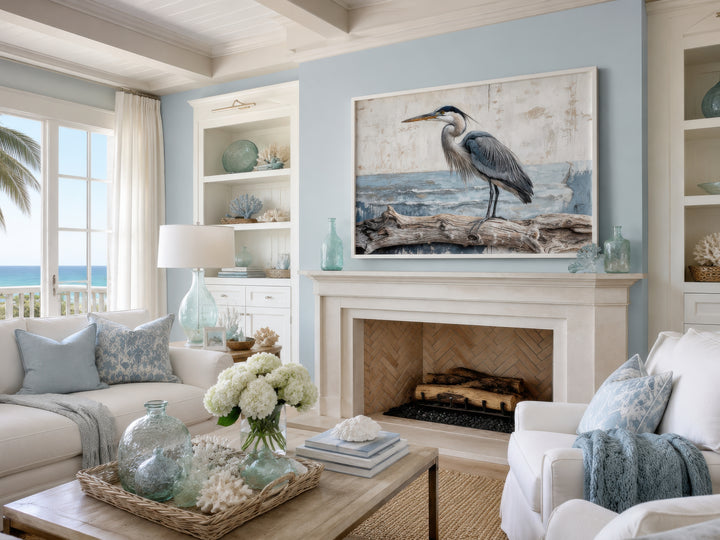 Coastal heron on driftwood canvas print above a fireplace in a serene blue and white living room.