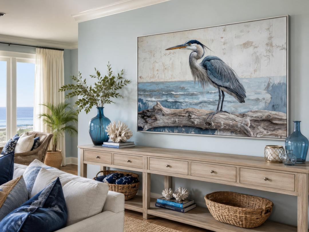 Large canvas print of a blue heron on driftwood above a wooden console table in a coastal room.