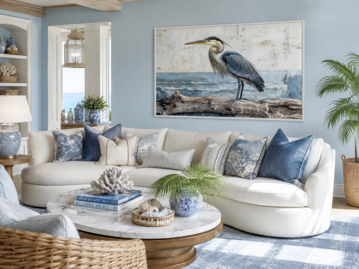 Coastal heron on driftwood canvas wall art in a blue living room with a white sofa and marble table.