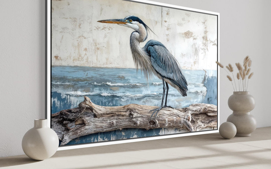 A framed canvas print of a blue heron on driftwood, displayed in a serene coastal-themed room.