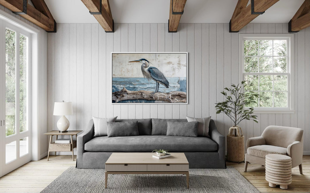 A large canvas print of a coastal heron on driftwood hangs in a bright, rustic living room.