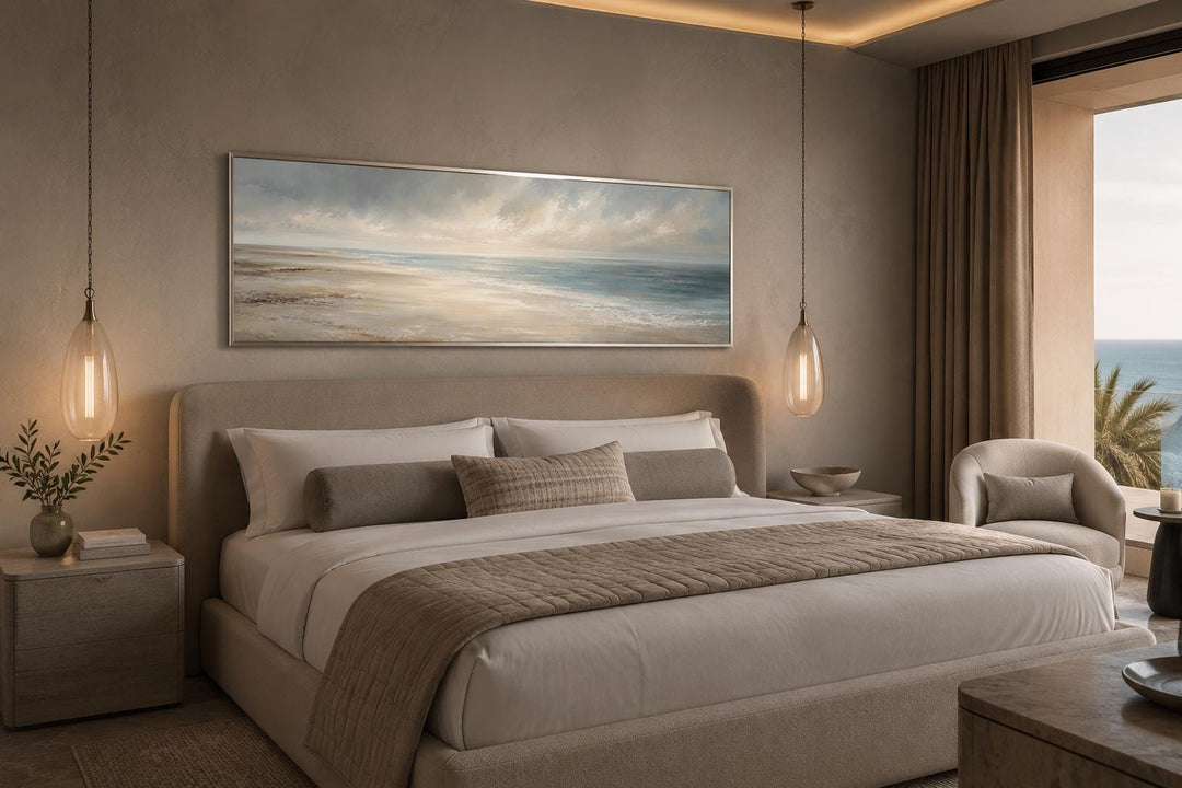 Long horizontal coastal wall art of a calm ocean seascape hanging above a neutral bed.