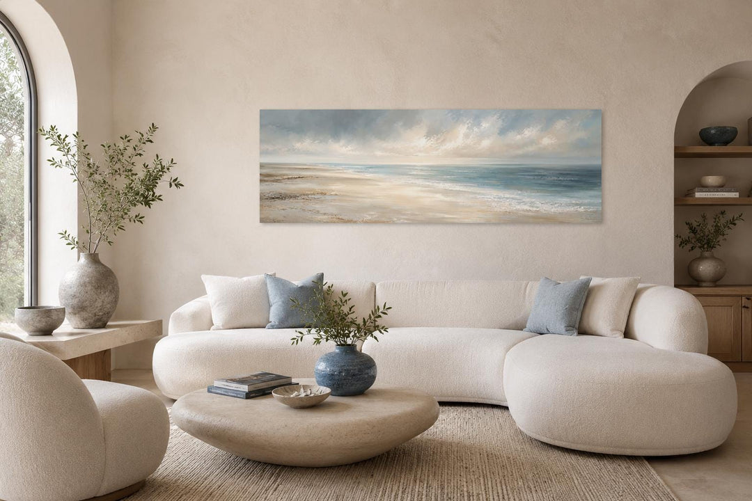 Long horizontal coastal wall art canvas featuring a soft ocean seascape above a neutral sofa.