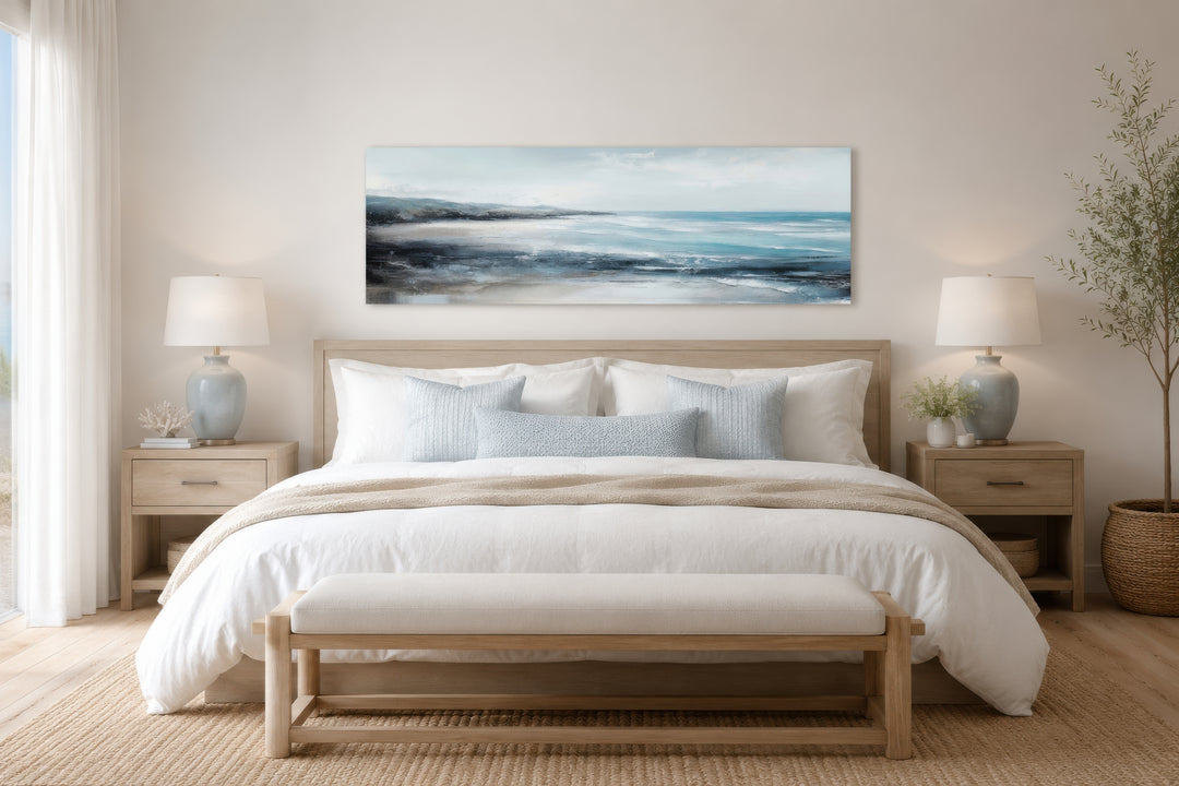 Long narrow coastal wall art featuring a serene ocean beach scene hanging over a bed.