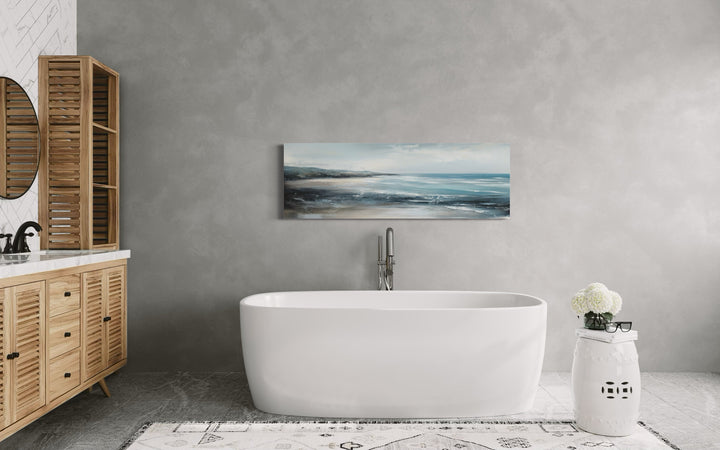Long narrow coastal canvas wall art featuring a serene ocean beach scene above a white bathtub.