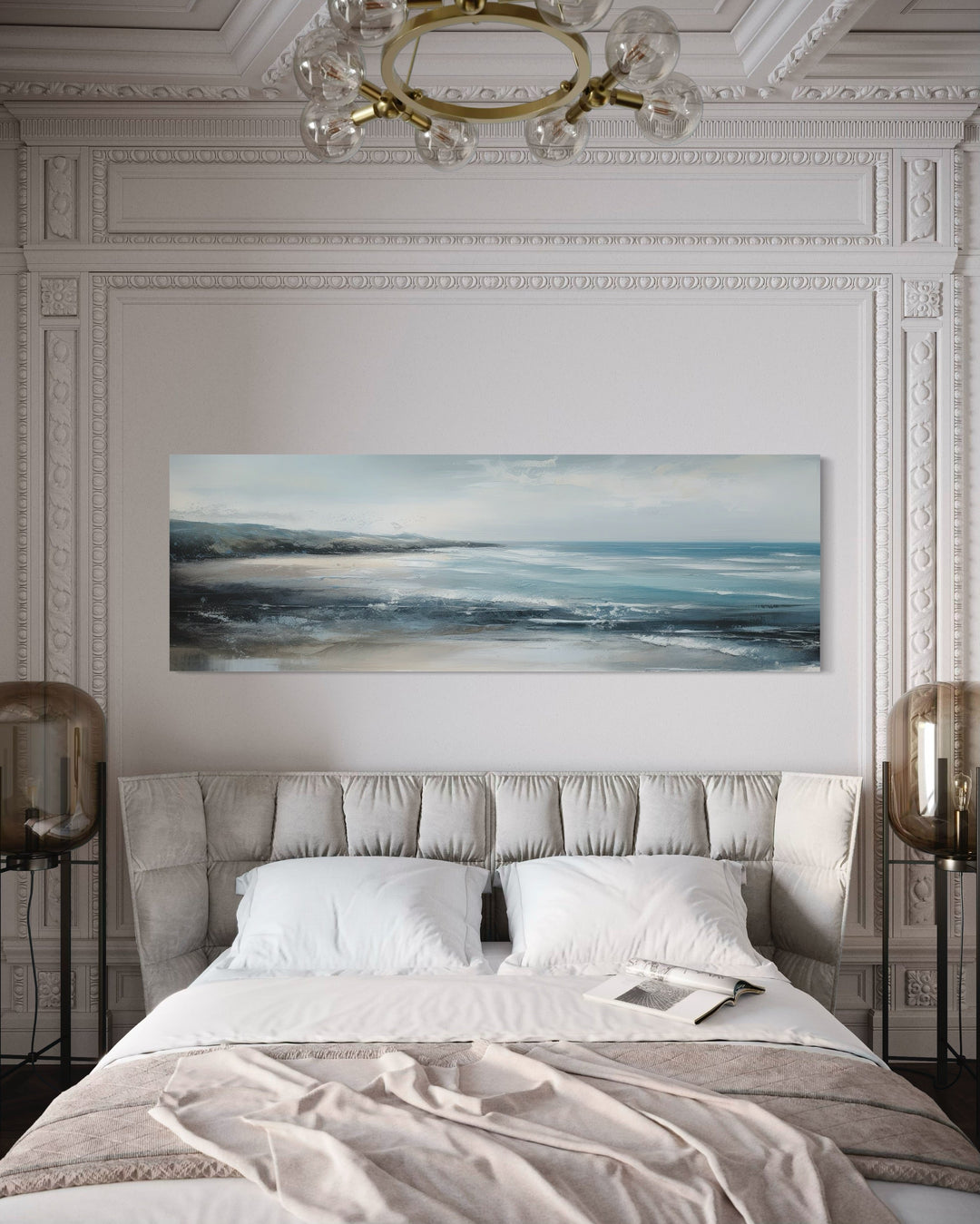 Long narrow coastal canvas art of a blue ocean and sandy beach hanging over a bed.