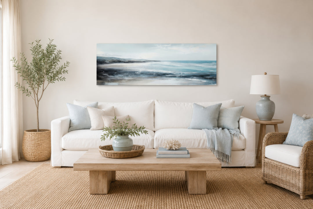 Long narrow coastal wall art featuring a serene ocean beach scene above a white sofa.