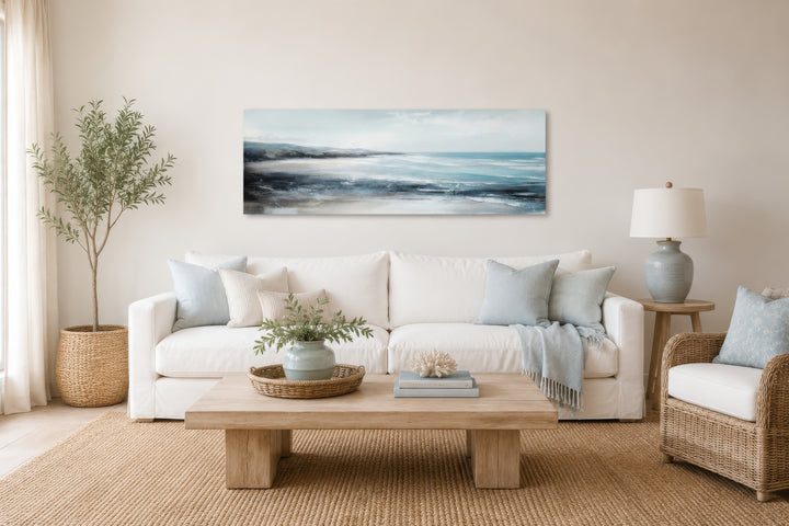 Long narrow coastal wall art featuring a serene ocean beach scene above a white sofa.