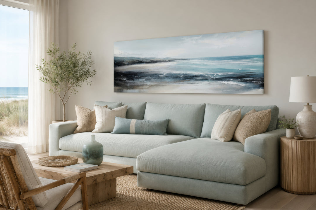 Long narrow coastal wall art of an ocean beach scene hanging over a light blue sectional sofa.
