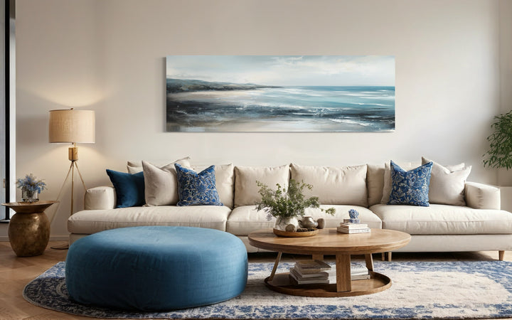 Long narrow coastal wall art featuring a serene ocean beach scene above a modern sofa.