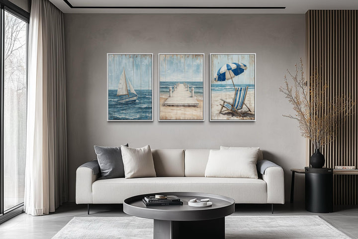 Three-piece coastal wall art set featuring a sailboat, pier, and beach chair above a modern sofa.